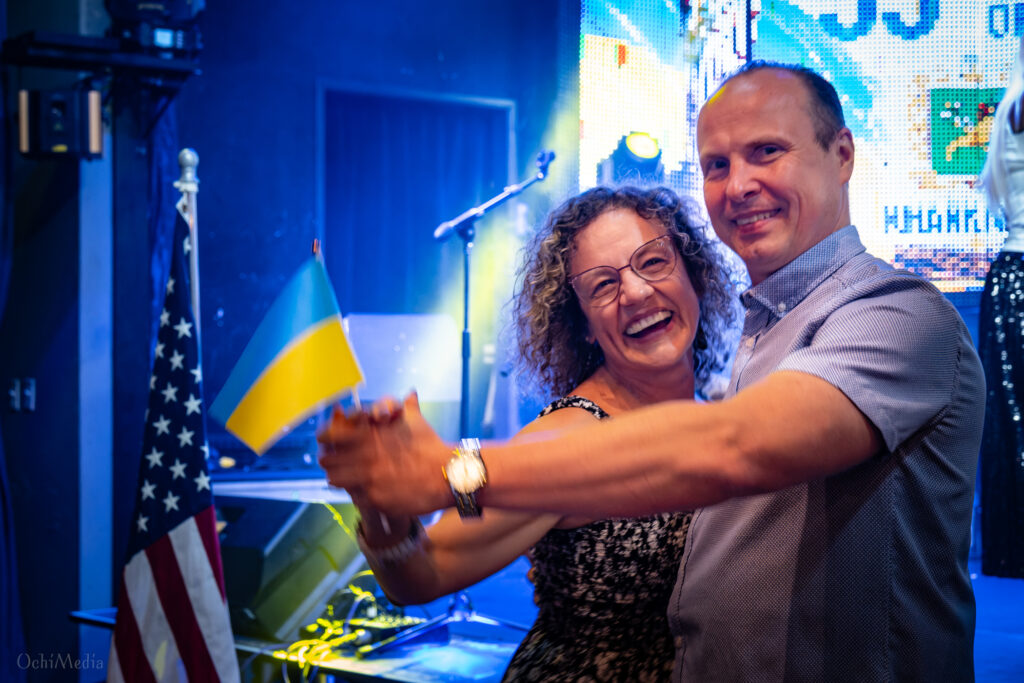 A couple dances during a Ukrainian Independence Day celebration in North Texas, with Ukrainian and American flags in the background.